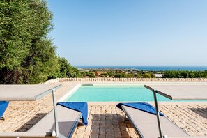 Zona junto a la piscina con dos sillas reclinables y vista al mar.