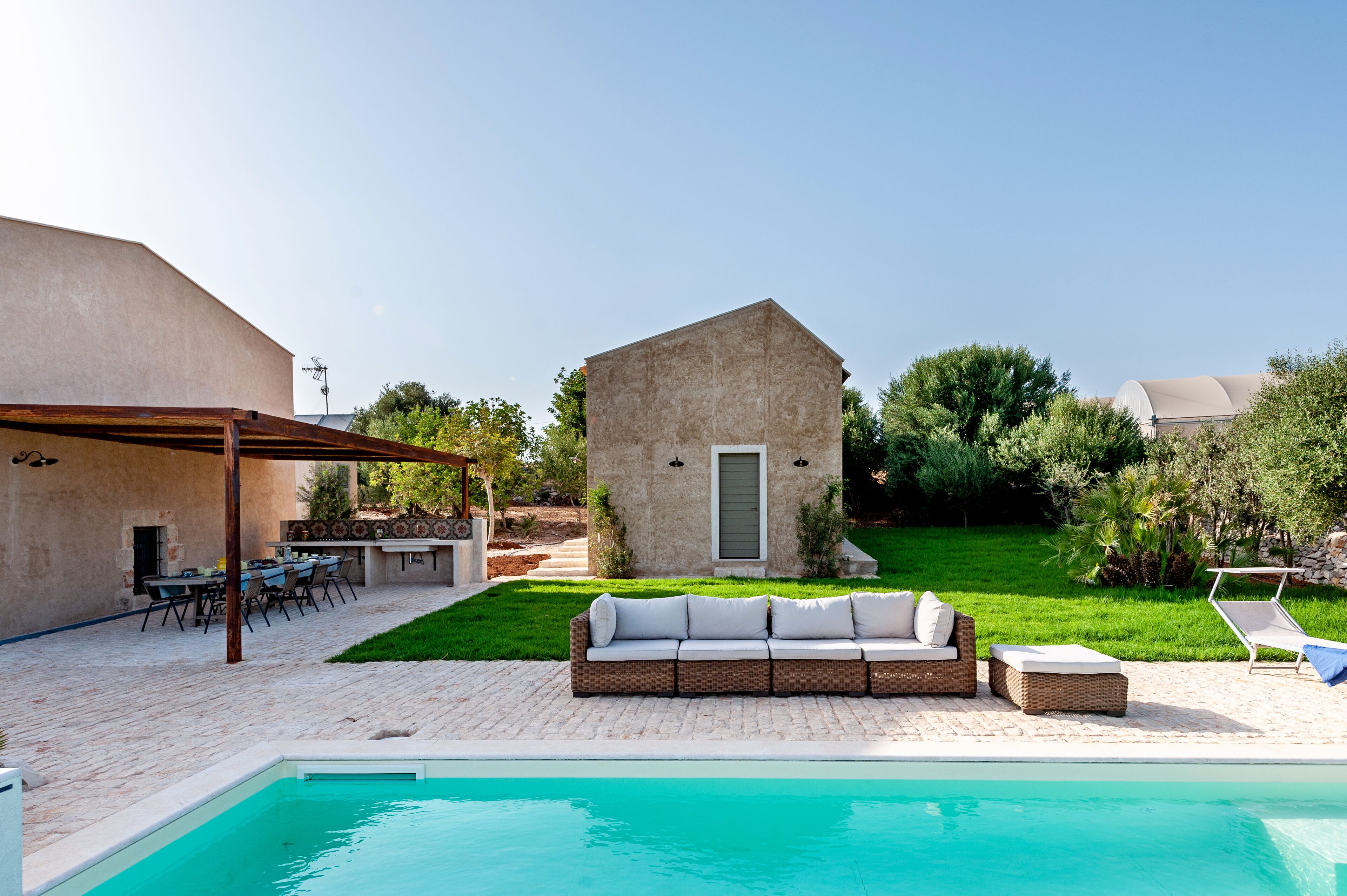 A poolside area with a built-in sofa, a barbecue setup, and a small building in the background.