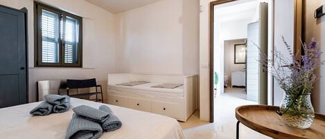A bedroom with a bed, a chair, a bedside table with a vase, and a window with blinds.