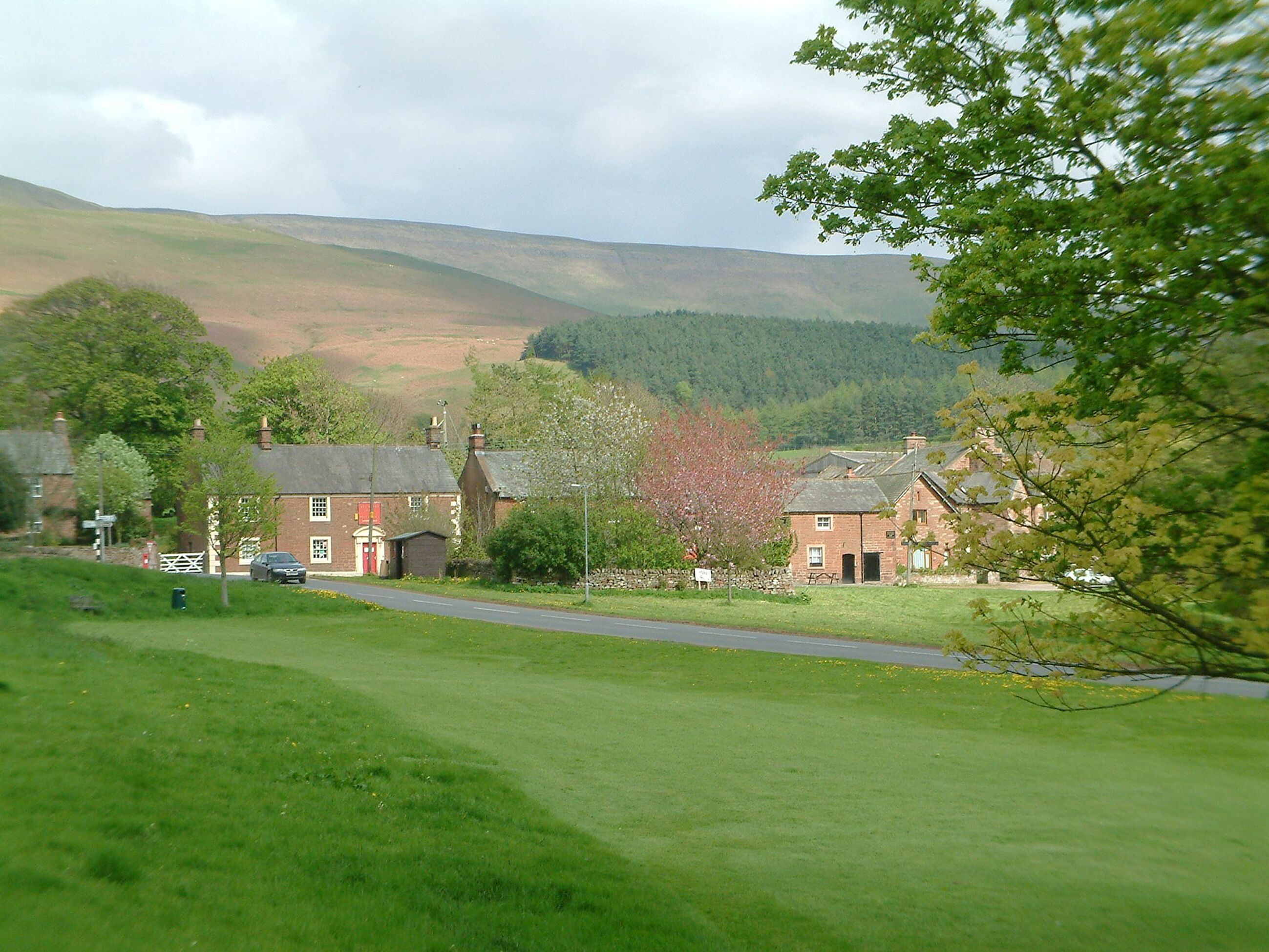 A rural landscape with a road, a red brick building, and a green field.