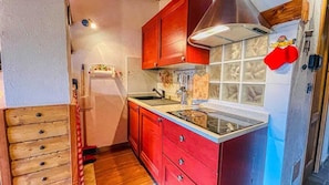 Una cocina compacta con armarios de madera, un ventanal y una puerta roja.