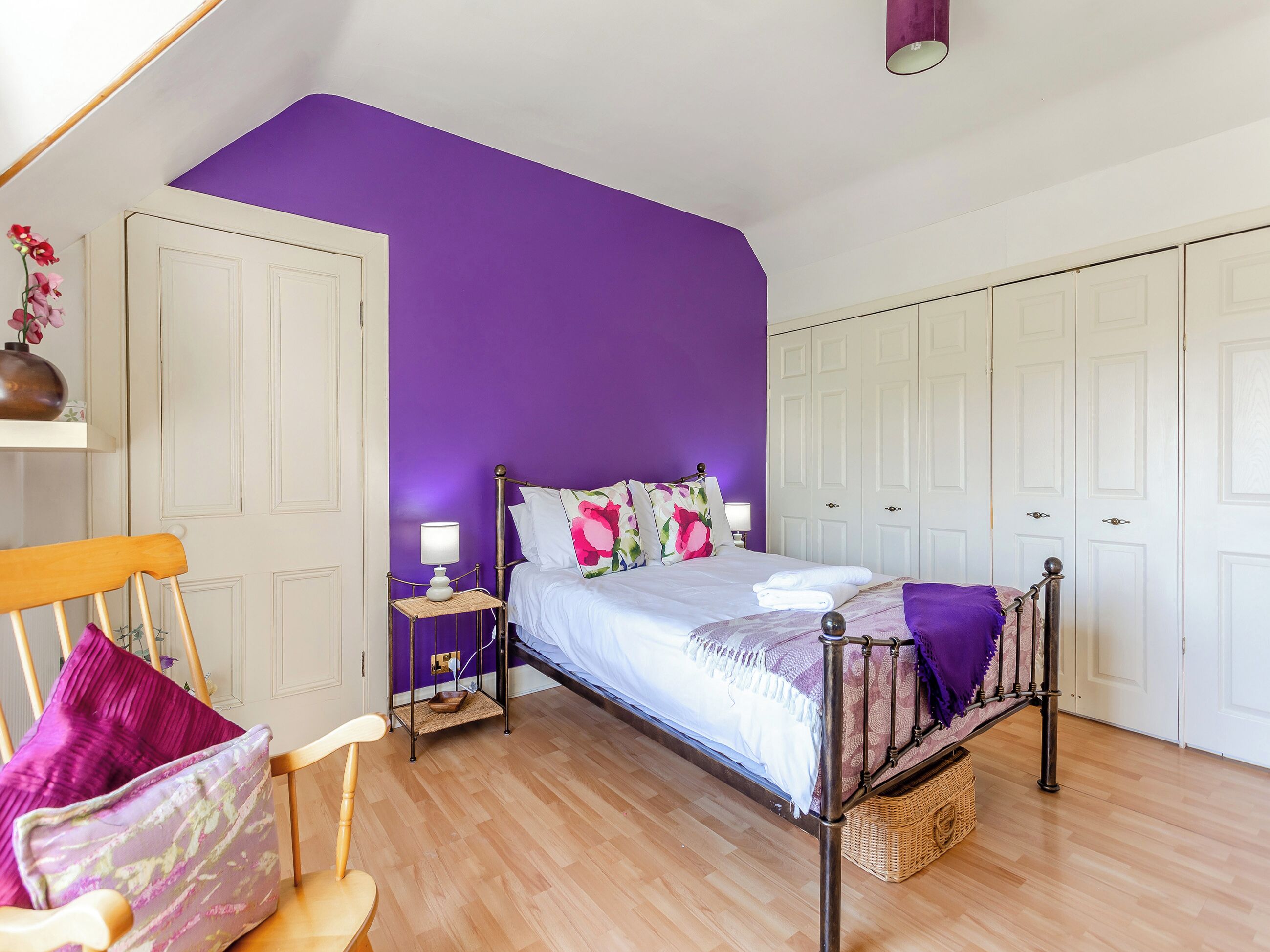 A bedroom with a bed, a nightstand, a chair, a wardrobe, and a ceiling light.