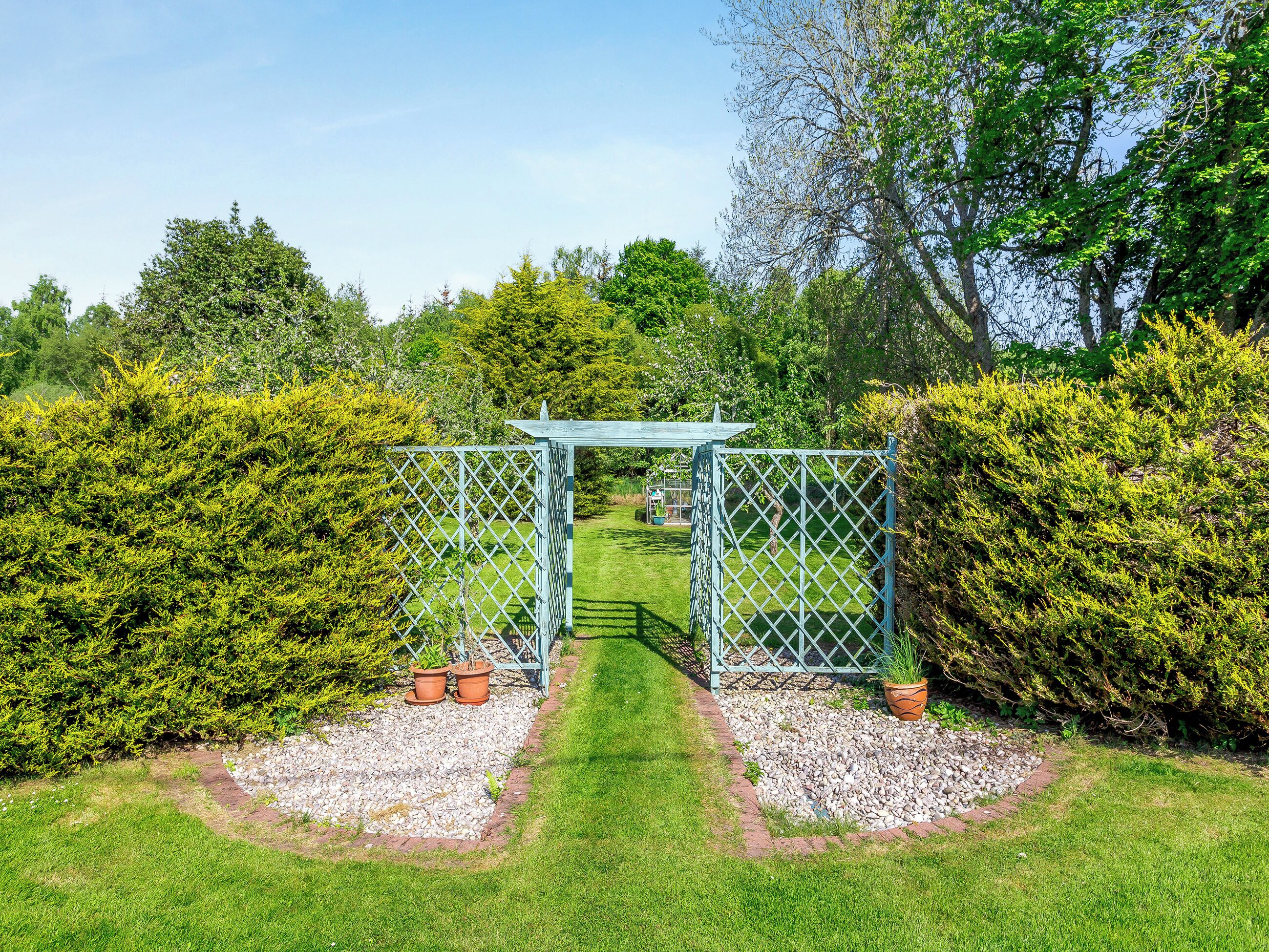 A garden with a metal gate, gravel paths, and green hedges.