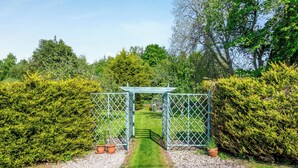 Ein Garten mit einem Metallzaun, Kieswegen und grünen Hecken.