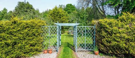 A garden with a metal gate, gravel paths, and green hedges.