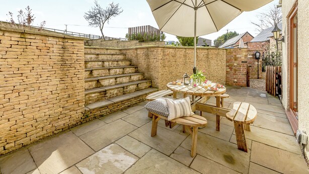 Un patio con una mesa y sillas, un parasol grande y un muro de piedra con escalones.