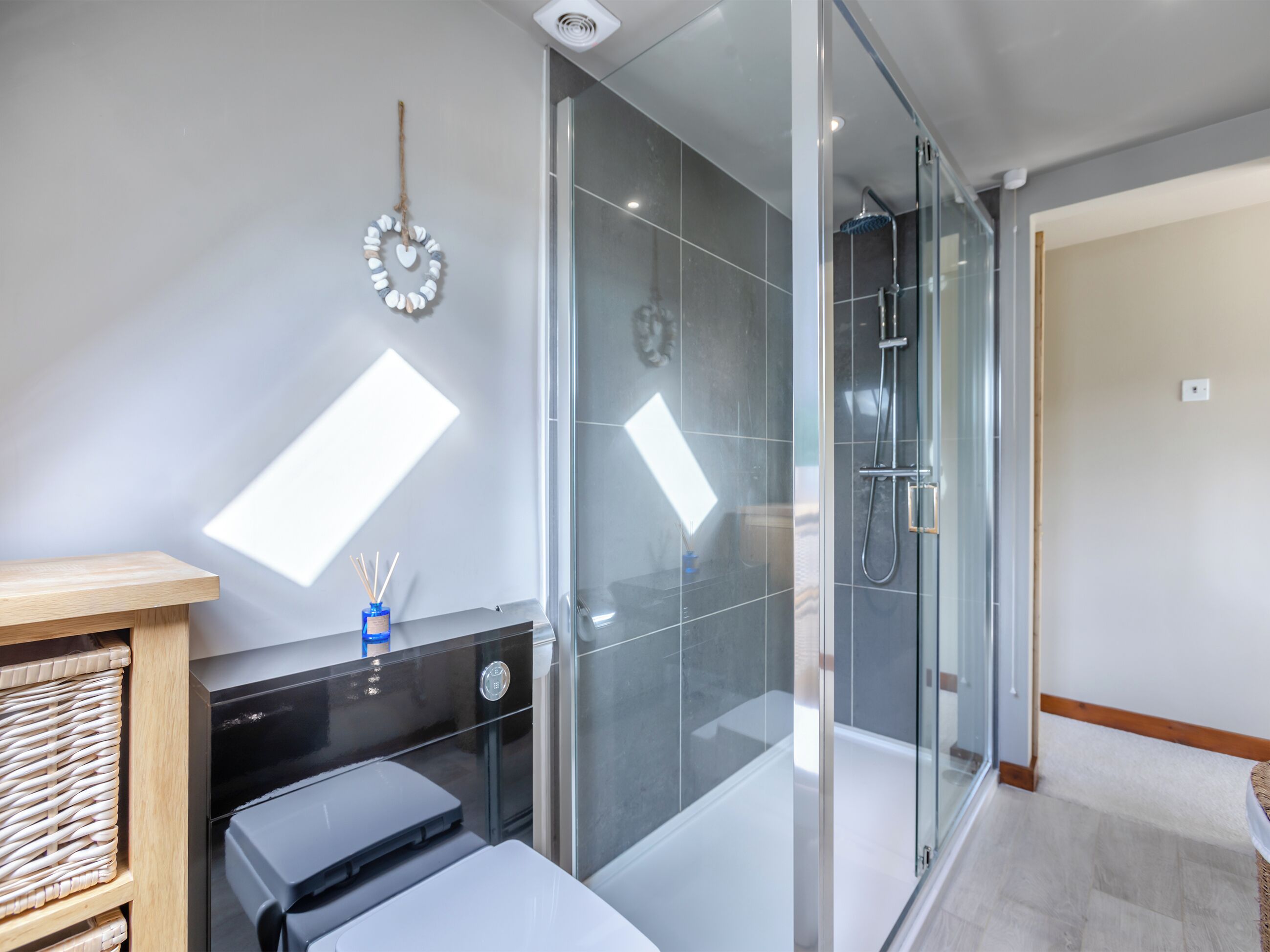 Un baño moderno con cabina de ducha de vidrio, un banco de madera, una mesita con un recipiente azul y un reloj en la pared.