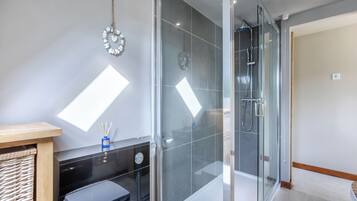 Un baño moderno con cabina de ducha de vidrio, un banco de madera, una mesita con un recipiente azul y un reloj en la pared.