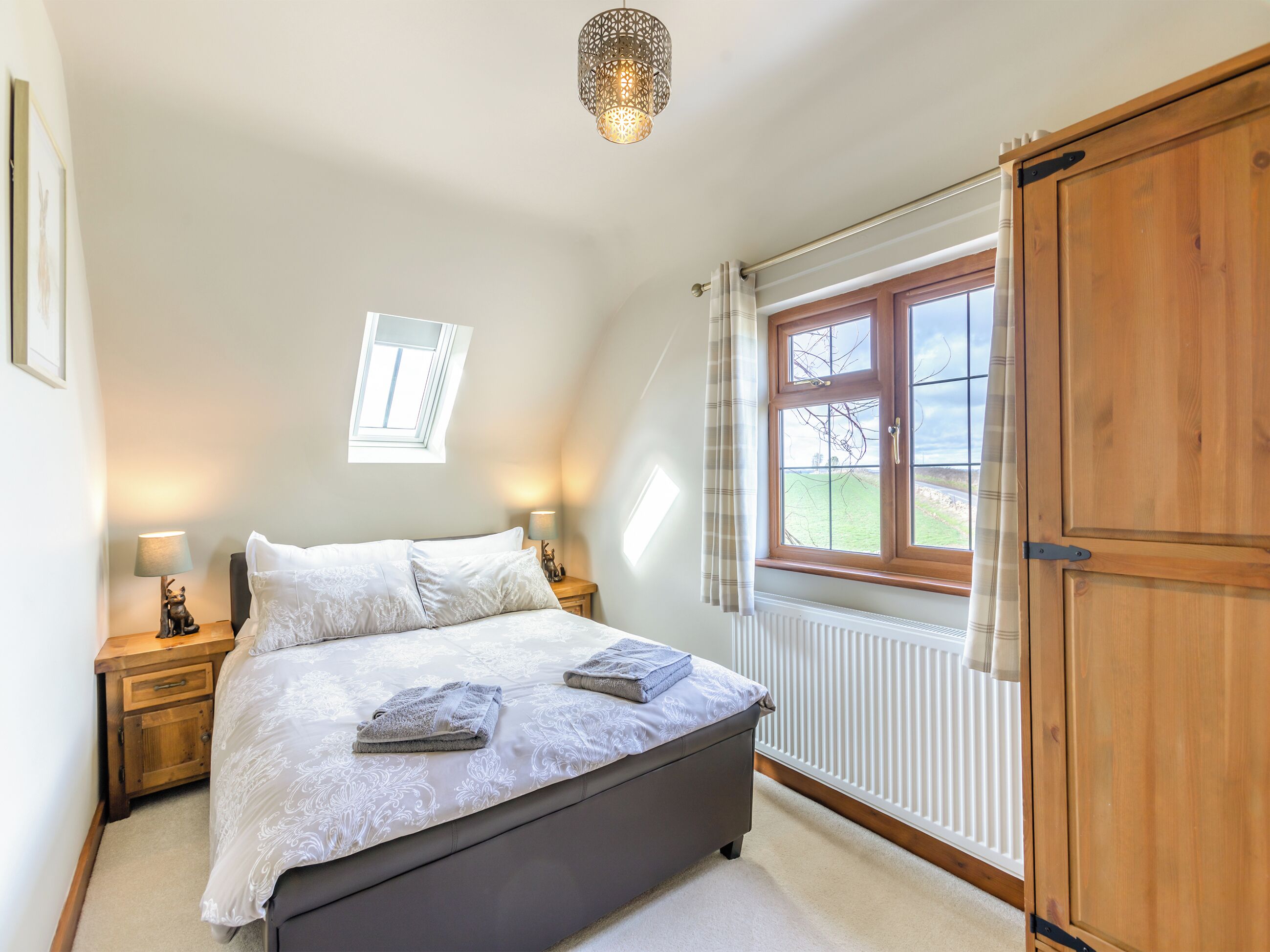 A bedroom with a bed, bedside lamps, a window, a radiator, and a wardrobe.