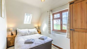 A bedroom with a bed, bedside lamps, a window, a radiator, and a wardrobe.