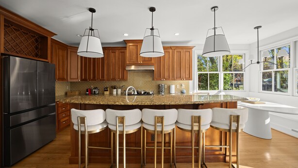 Cocina moderna con armarios de madera, refrigerador de acero inoxidable, encimera de granito y barra con taburetes.