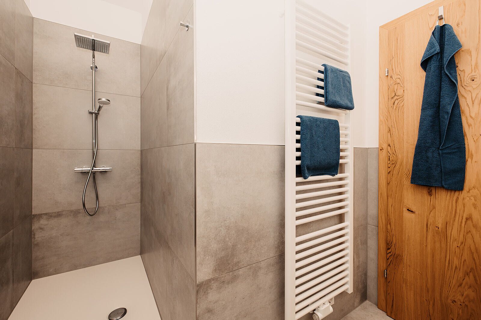 A modern bathroom with a shower, a towel rack, and a wooden door.