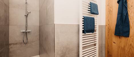 A modern bathroom with a shower, a towel rack, and a wooden door.