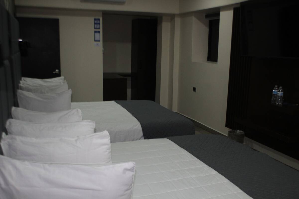 Habitación de hotel con dos camas, una kitchenette pequeña y un televisor.