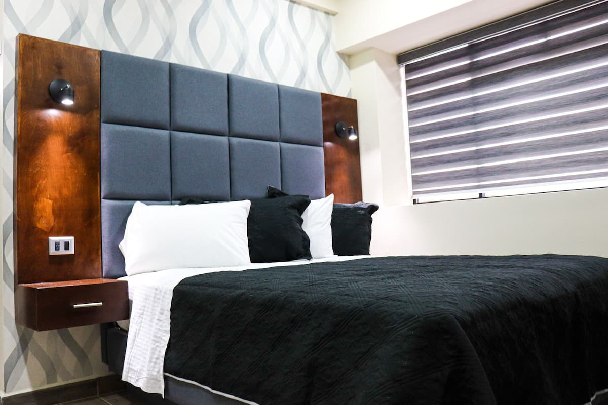 Una habitación de hotel moderna con una cama grande, una mesita de noche de madera y una ventana con persianas.
