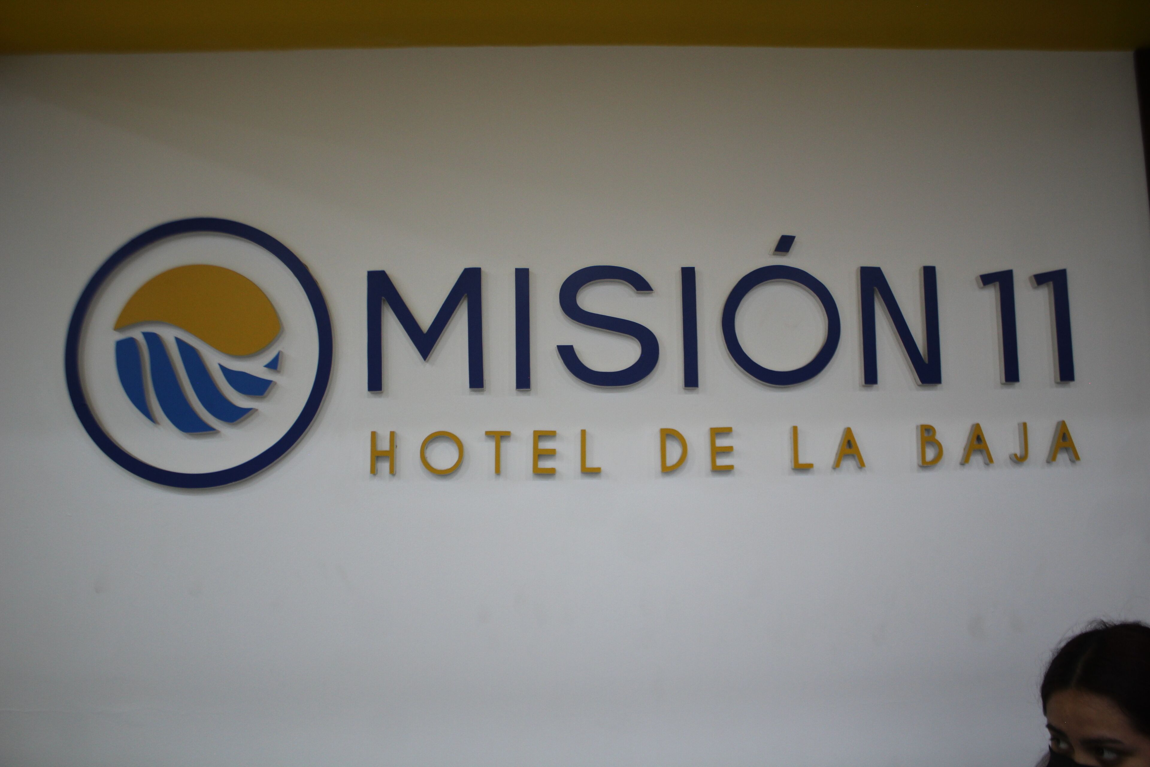 Un letrero que dice 'Misión 11 Hotel de la Baja' con un logotipo que muestra un diseño estilizado de olas y un sol.