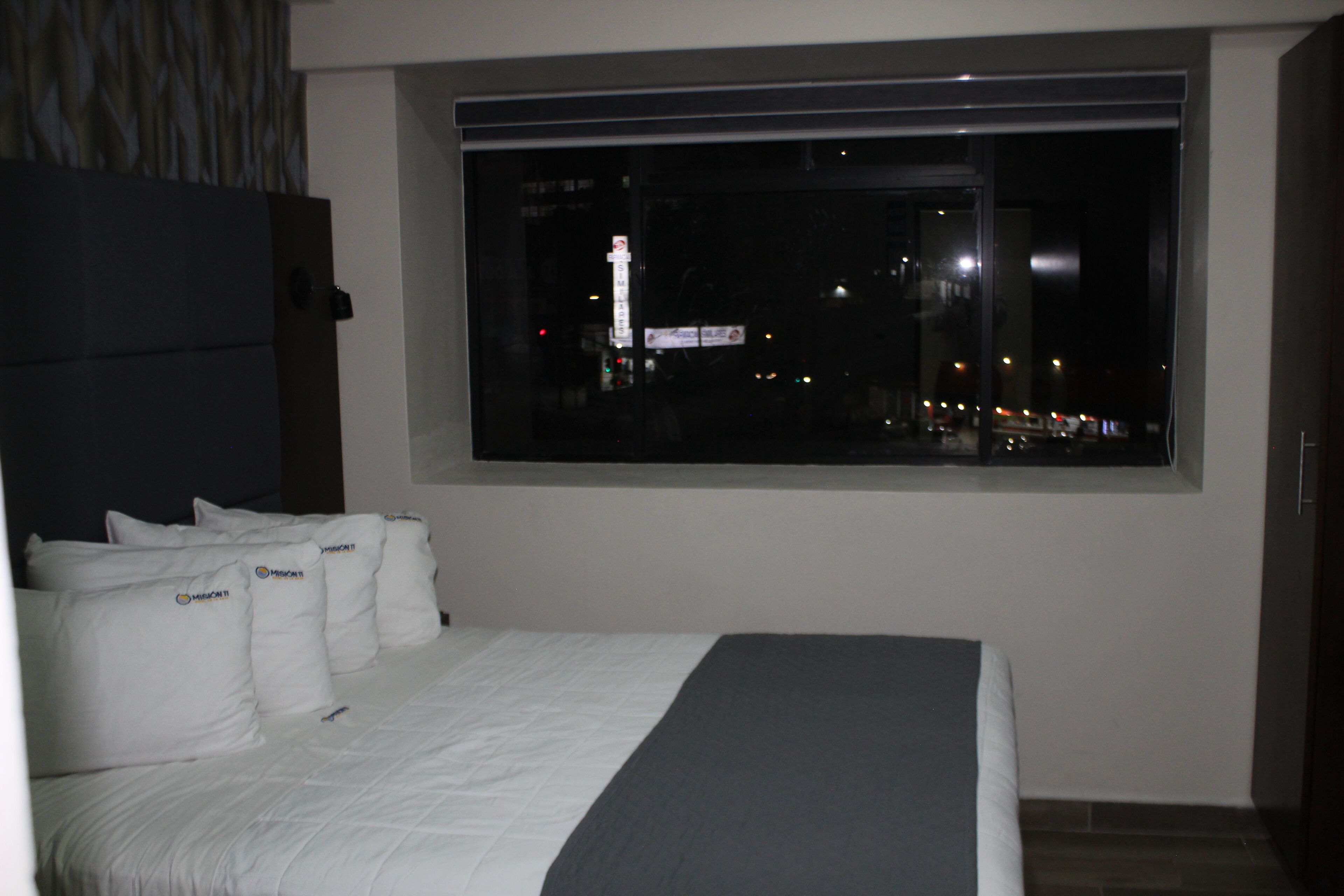 A bedroom with a large window, a bed with white bedding, and a dark headboard.