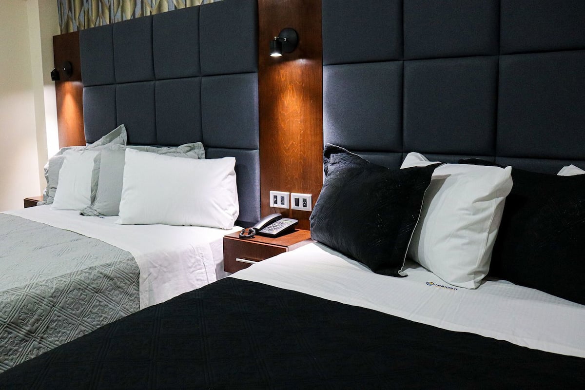 Habitación de hotel con una cama grande, una mesita de noche con teléfono y un cabecero con lámpara.