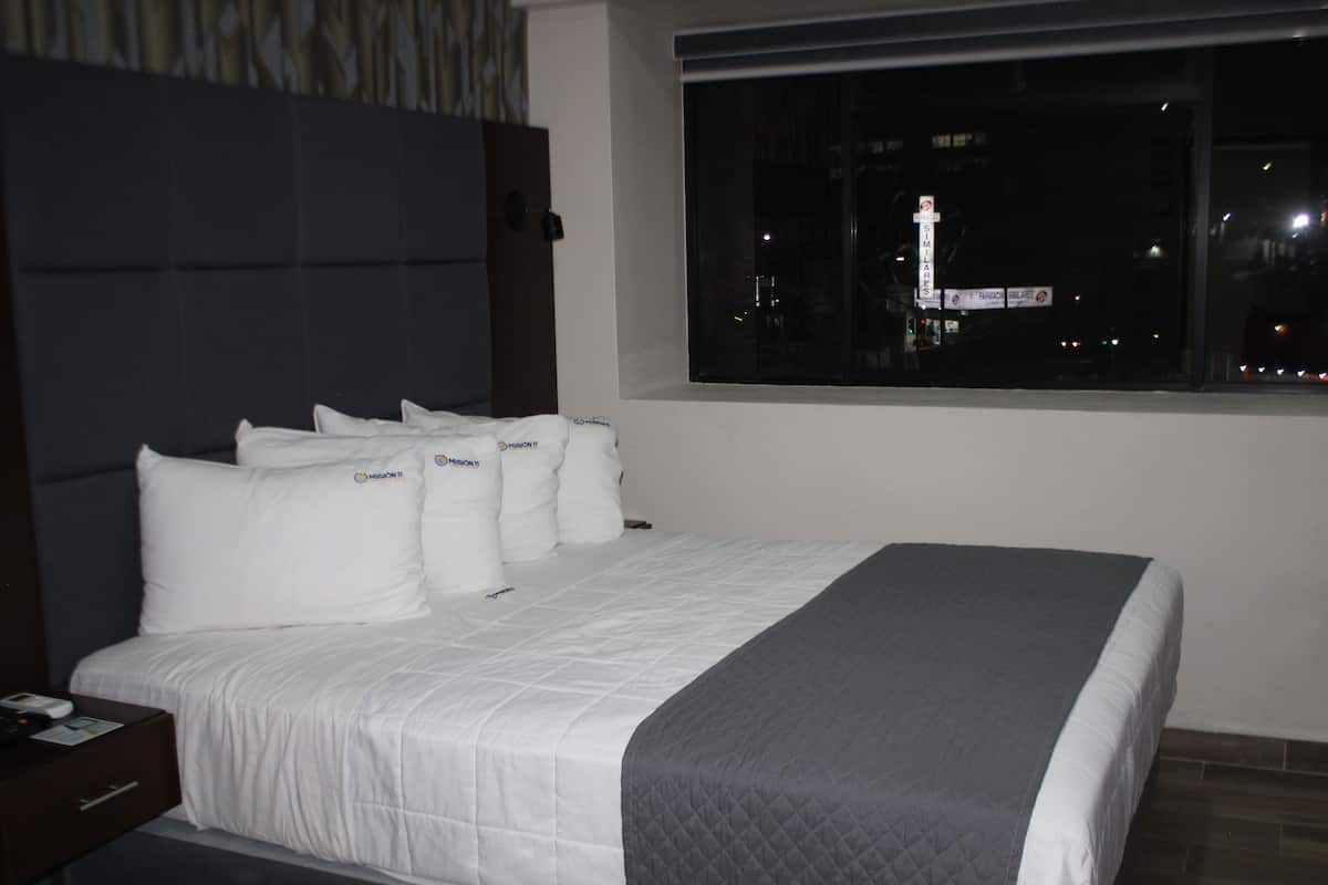Una cama bien hecha con ropa de cama blanca y una manta gris.