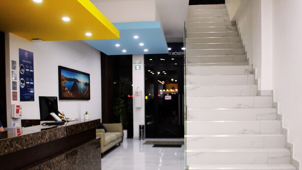 A hotel reception area with a marble staircase, a reception desk, and a wall-mounted TV. - MISION 11 (Tijuana)