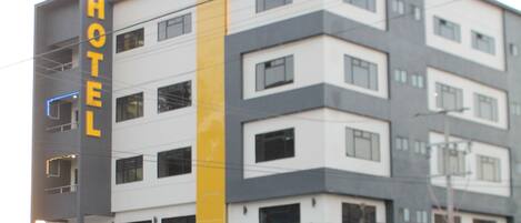 Un hotel de varios pisos con un llamativo letrero que dice 'HOTEL' en la fachada, un letrero 'MISSION 11' sobre la entrada y un diseño arquitectónico moderno con una pared de acento amarilla.