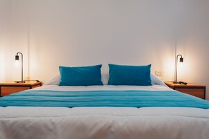 Una cama bien hecha con cubrecama y dos almohadas azules, flanqueada por dos mesitas de noche con lámparas.
