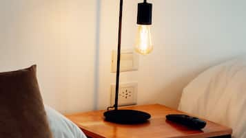A neatly made bed with a brown pillow, a wooden bedside table with a black lamp, and a remote control on the table.