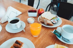 Una escena de desayuno con una mesa de madera, tostadas, mantequilla, mermelada, un vaso de jugo de naranja, una taza de café y un mantel con vasos.