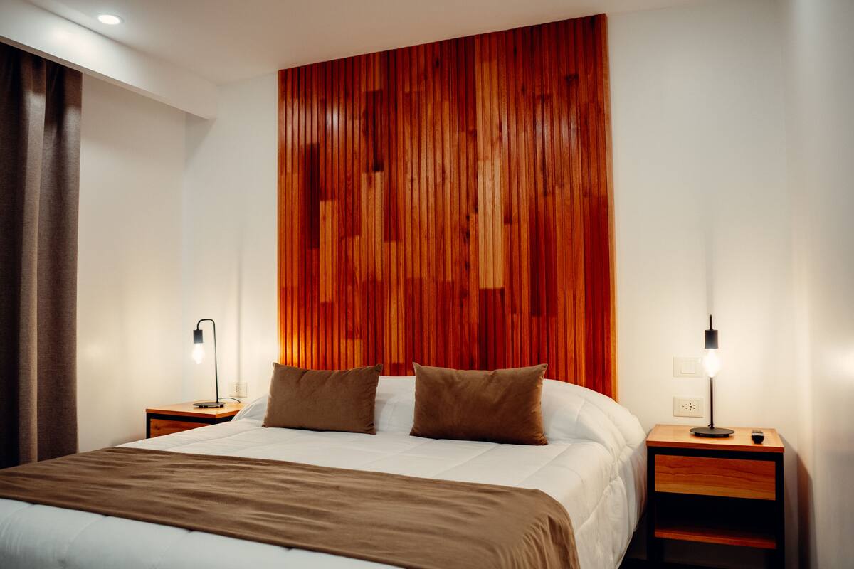 A hotel room with a large bed, two bedside tables, and a wooden accent wall.