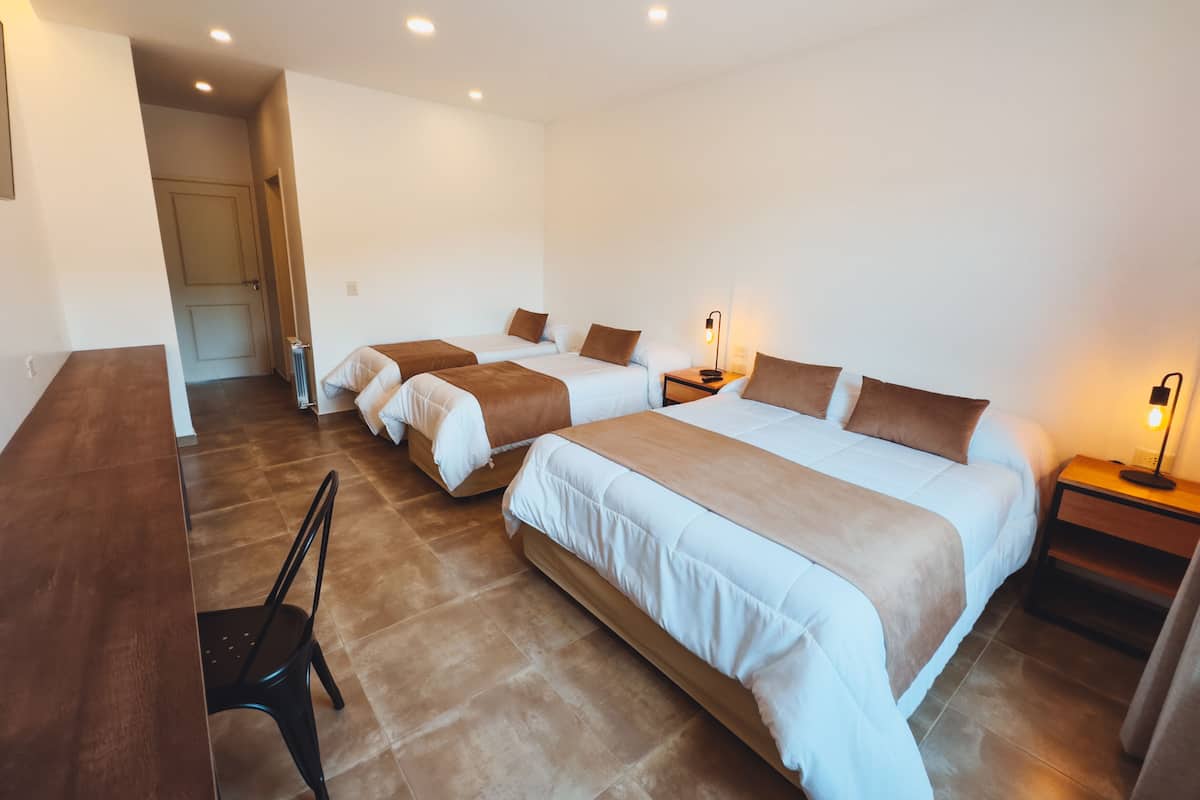 A hotel room with three beds, a desk, and a chair.