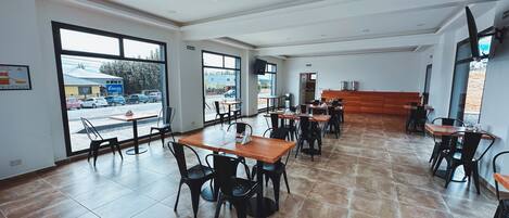 Un restaurante espacioso con techos altos, ventanas amplias y suelo de baldosas.
