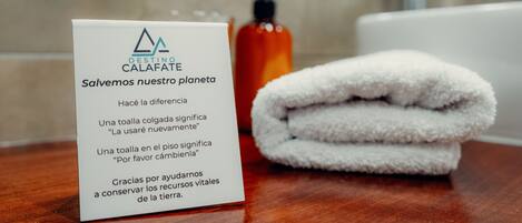 Un letrero con un logotipo y texto en un baño, una toalla blanca doblada y una botella de líquido anaranjado.