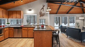 A spacious kitchen with wooden cabinets, a central island, and a dining area with a sofa and chairs. - 12 Quartz Mtn - Updated and Classy! Pickleball, SHARC, Fireplace, Backs to Sunriver Forest (Sunriver)