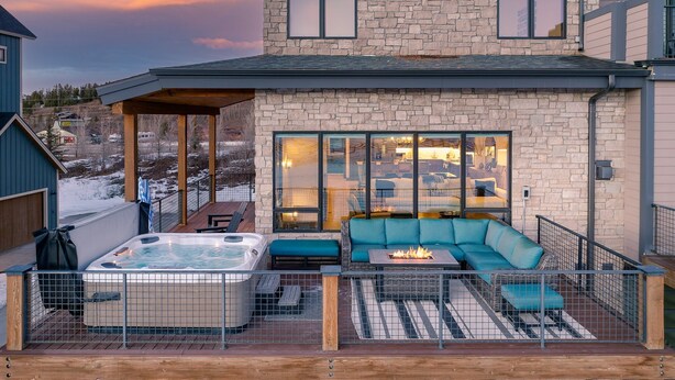 Ein modernes Haus mit Natursteinaußenwand, einer überdachten Terrasse mit Whirlpool und einer gemütlichen Sitzecke.