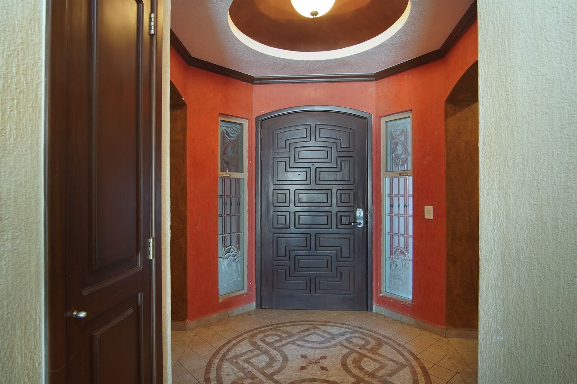 A hallway with a dark wooden door, red walls, and a patterned floor.