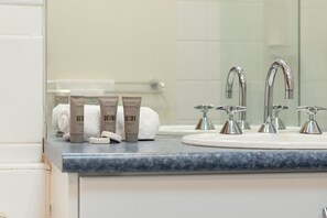A bathroom with a marble countertop, a white sink, and three bottles of shampoo and body wash. - StayCentral - Heritage Warehouse Retreat (Melbourne)