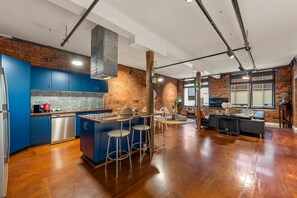 A modern kitchen with blue cabinets, a central island, and a dining area with a black sofa and bar stools. - StayCentral - Heritage Warehouse Retreat (Melbourne)