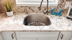 A kitchen with a stainless steel sink, white cabinets, and a window above the sink. - Welcome to Paradise Cove! - Steps From The Beach (Indian Shores)