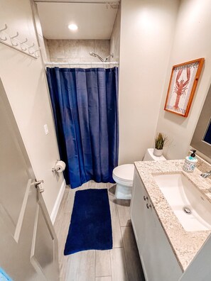 A bathroom with a shower, toilet, sink, and a blue shower curtain. - Welcome to Paradise Cove! - Steps From The Beach (Indian Shores)