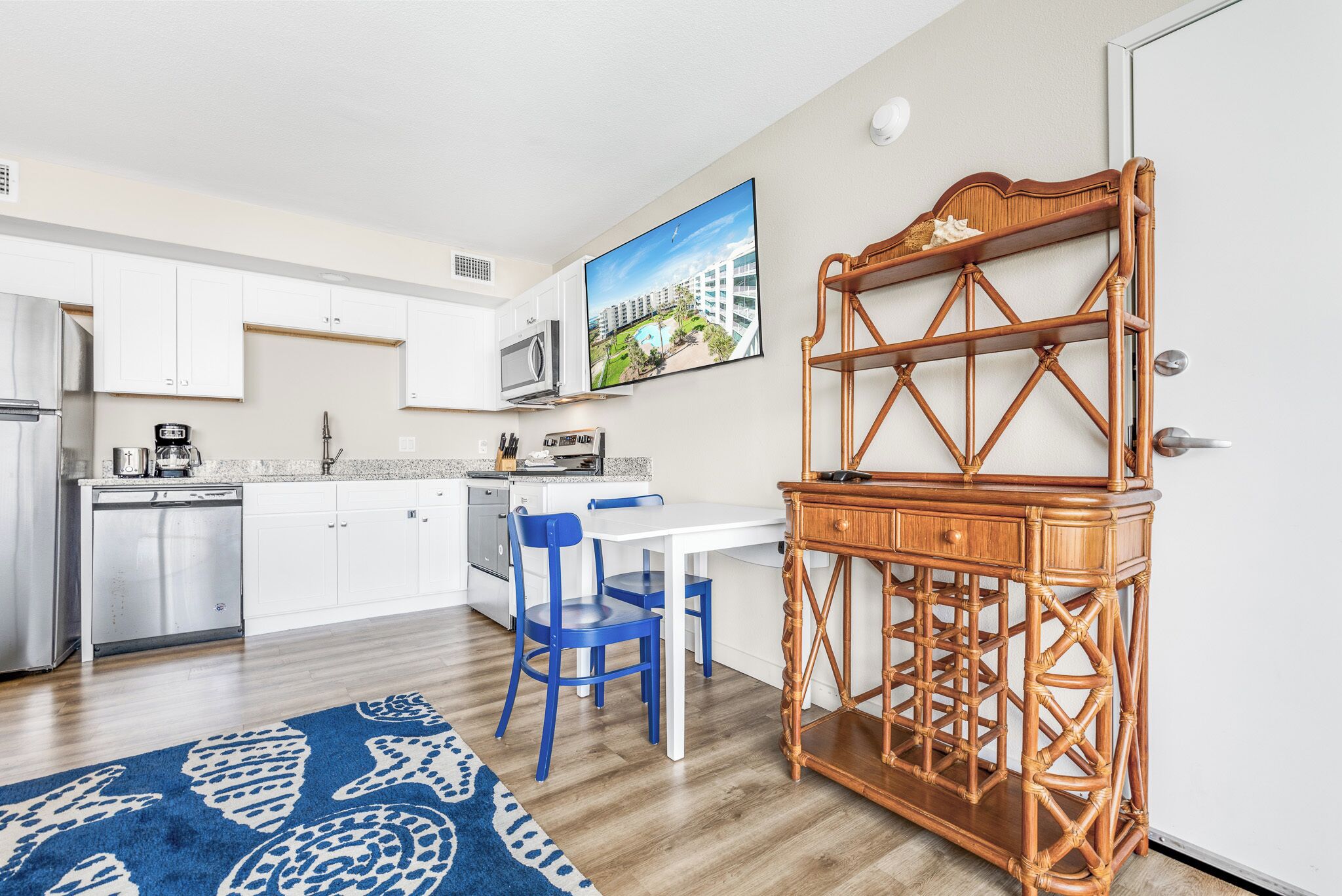 A modern kitchen with white cabinets, a stainless steel refrigerator, and a dining area with blue chairs.