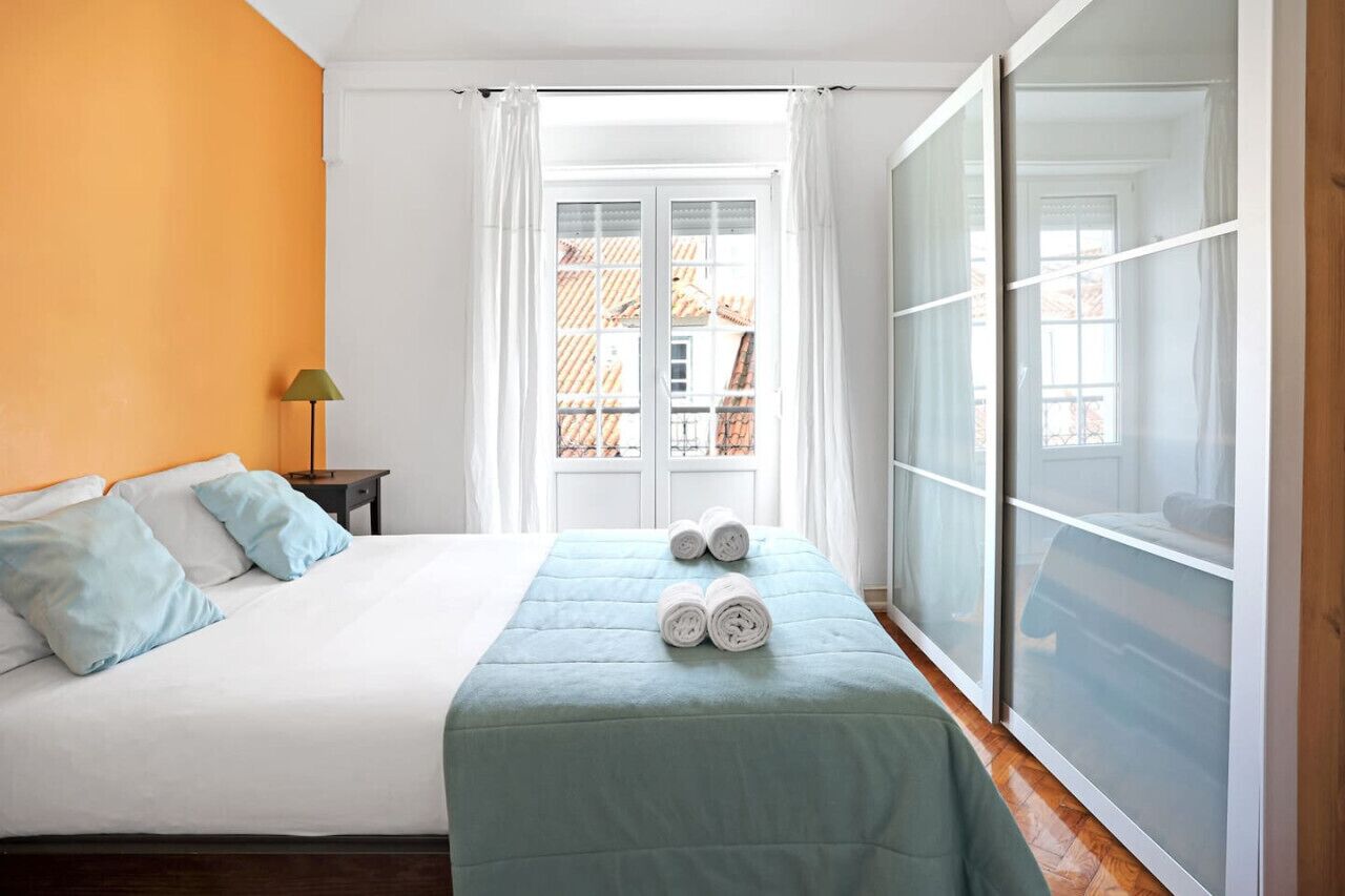A hotel room with a bed, a window with curtains, a lamp, and a view of buildings outside.