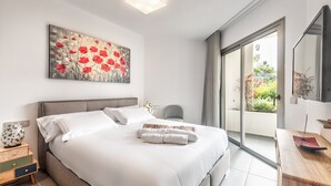 A modern bedroom with a large bed, a nightstand, a mirror, and a sliding glass door leading to a balcony. - Jardines - Tabor 0.2 POOL VIEW & GARDEN 1B (Arona)
