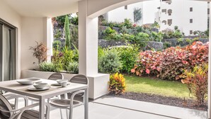 A patio with a dining table and chairs, surrounded by a garden with various plants and a stone wall. - Jardines - Tabor 0.2 POOL VIEW & GARDEN 1B (Arona)