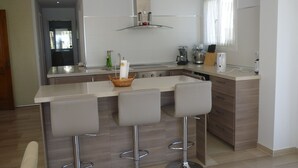 A modern kitchen with a central island, bar stools, stainless steel appliances, and a window providing natural light.