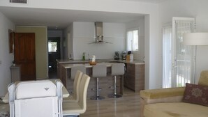 A modern kitchen with a central island, bar stools, and a dining area with a high chair.