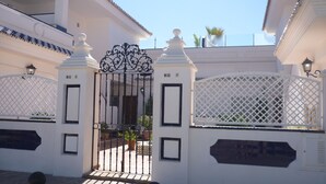 A gated entrance with a white wall and a decorative metal gate.