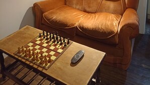 A room with a wooden ceiling, a brown leather sofa, a wooden coffee table with a chessboard, and a clock on the wall.