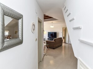 Een gang die uitkomt in een woonruimte met een bank, een televisie en een eethoek met een tafel en stoelen.