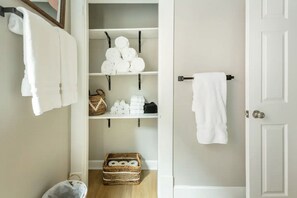 A bathroom with white towels hanging on hooks, a shelf with toiletries, and a basket on the floor.