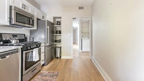 Una cocina con electrodomésticos de acero inoxidable, estufa, horno, microondas y refrigerador. Hay una alfombra estampada en el suelo.